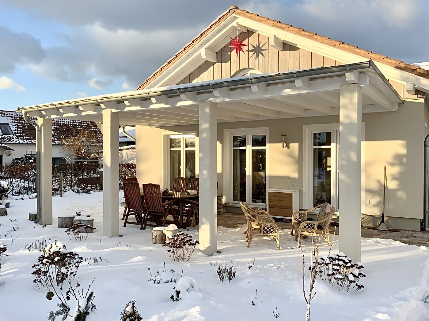 Terrace of a house with wooden table set and wicker furniture, snow in the front yard, sunny winter day.
