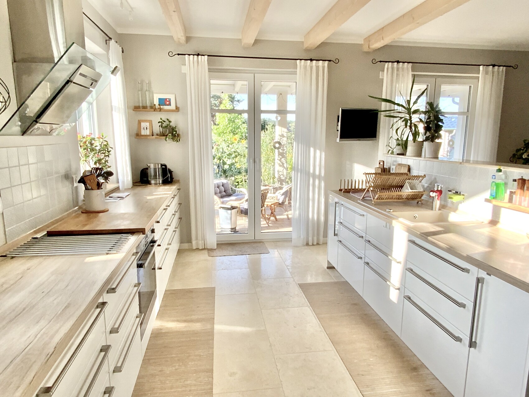 Bright kitchen with white cabinets, island, extractor hood, glass doors to the terrace and garden.