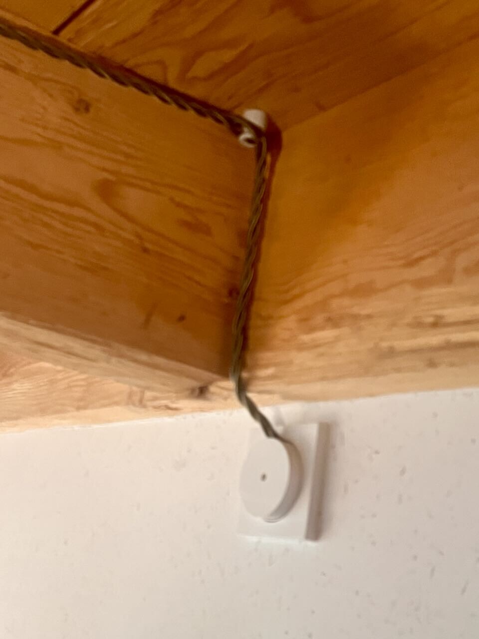 Cable runs over wooden beams to a white round switch on the wall.