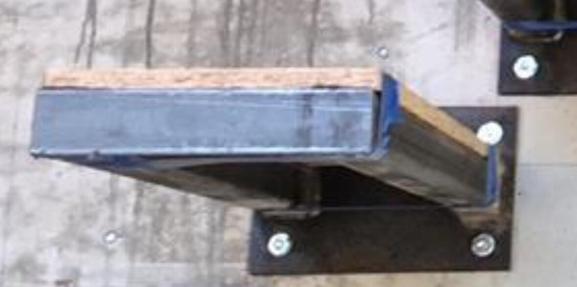 Blauer Metallblock mit Holzrand auf dunkler Holzplatte, festgeschraubt.
