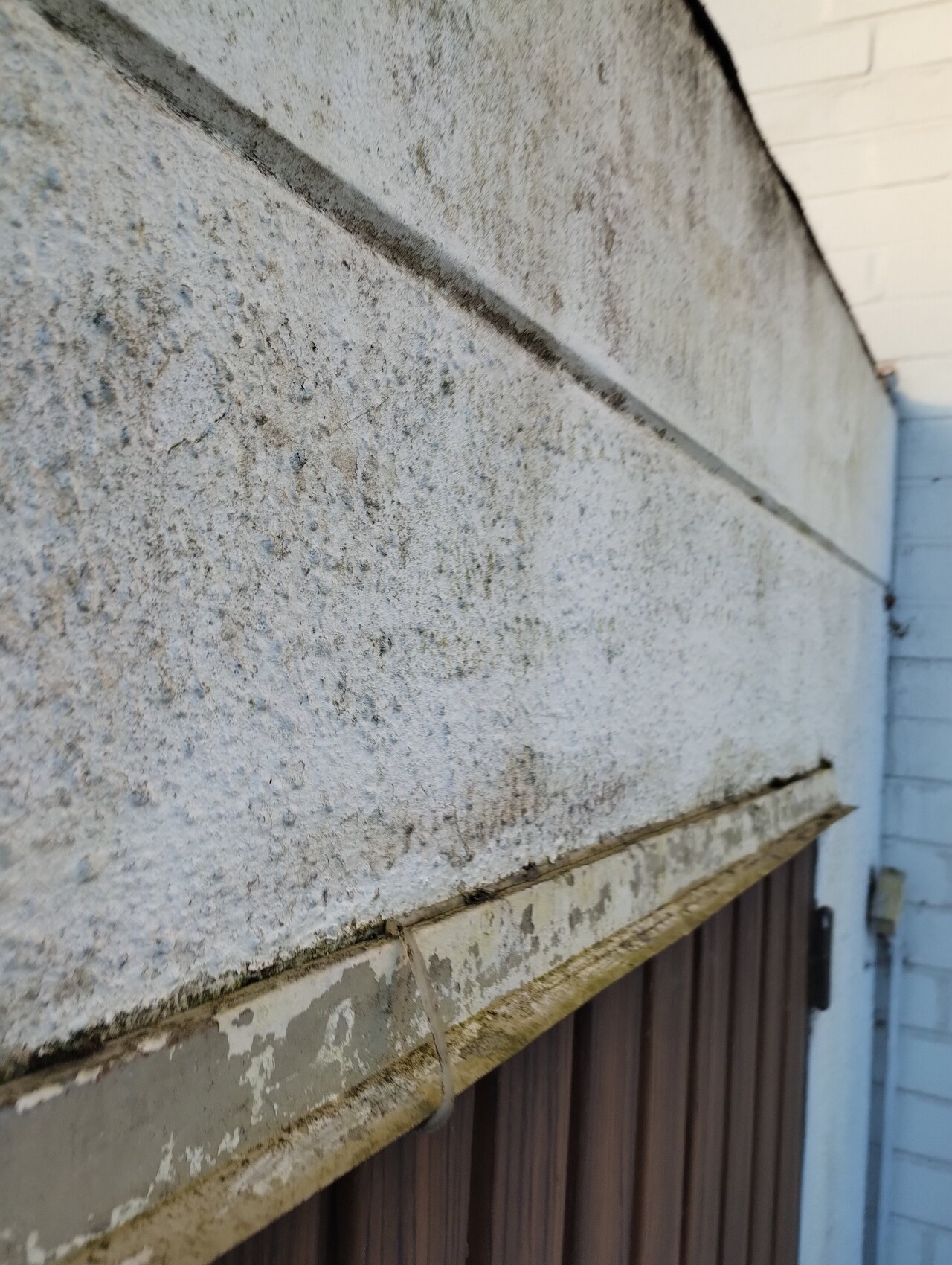 Coarse plastered exterior wall with horizontal joint; below peeling plaster on wooden boarding.