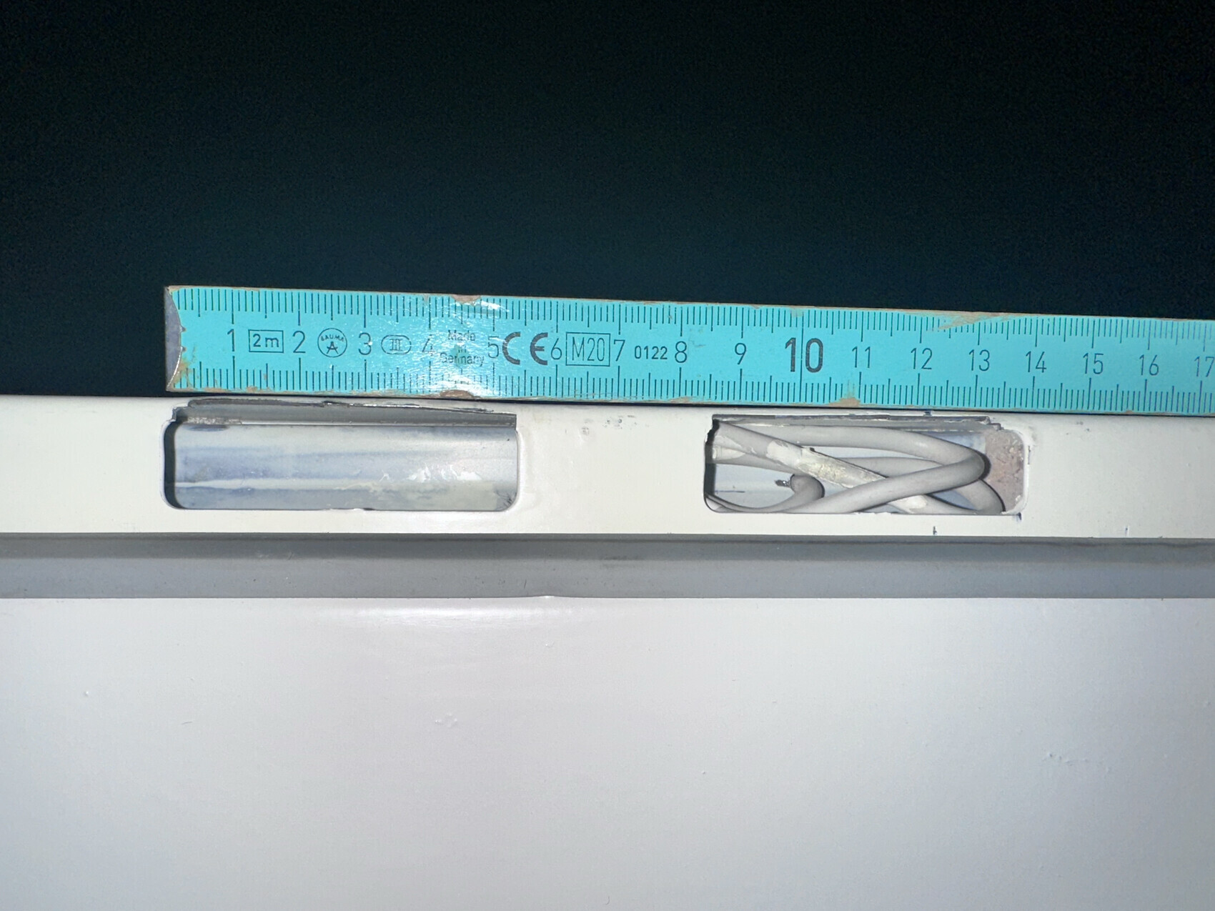 Blue tape measure lying on a white surface; cable visible in the slot on the right.