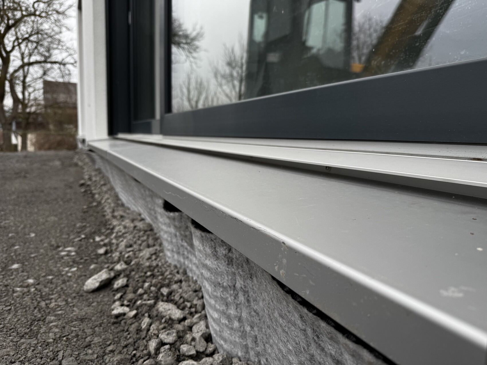 Exterior window with gray metal window sill, gravel ground and foundation visible
