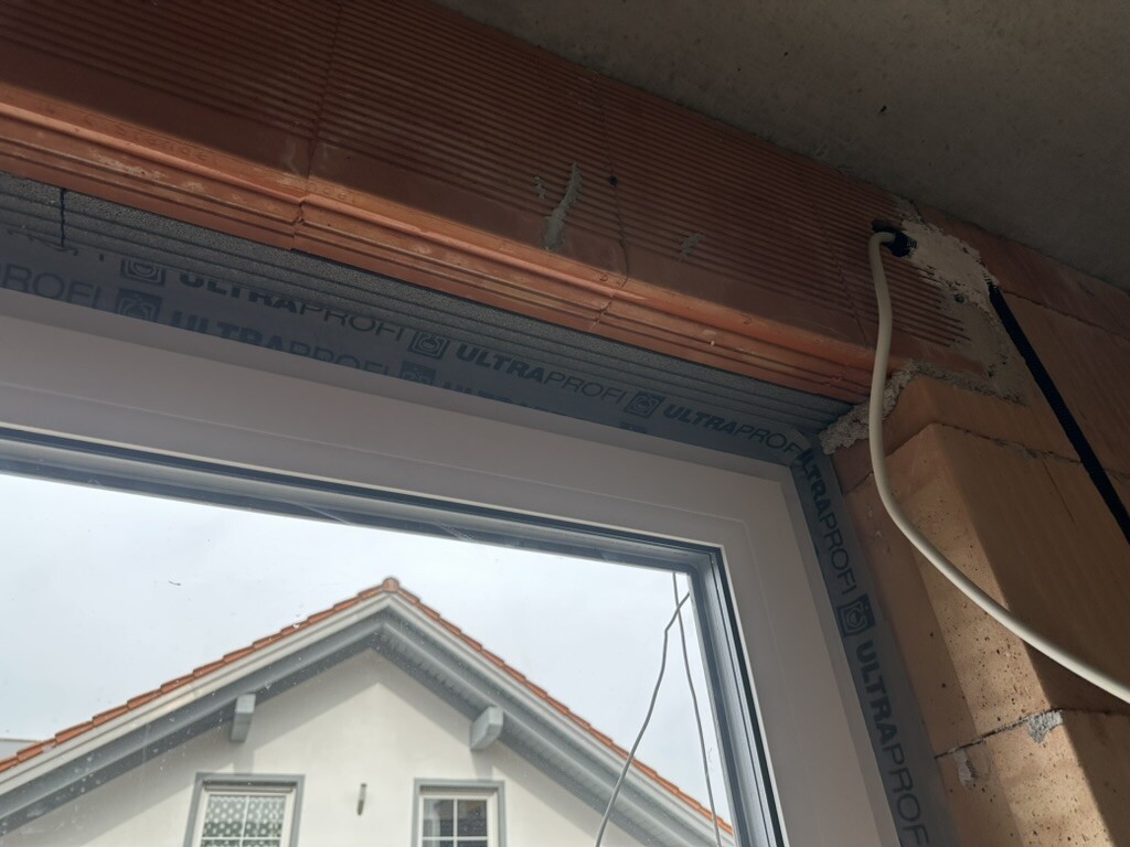 New window frame construction with ULTRAPROF sealing tape, cable at the wall, view of house with red roof.