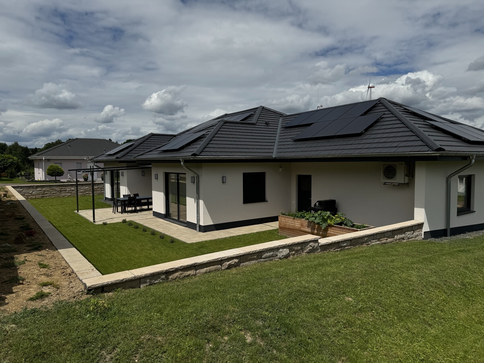Modern single-family house with solar modules on the roof, terrace with dining table and well-maintained garden.