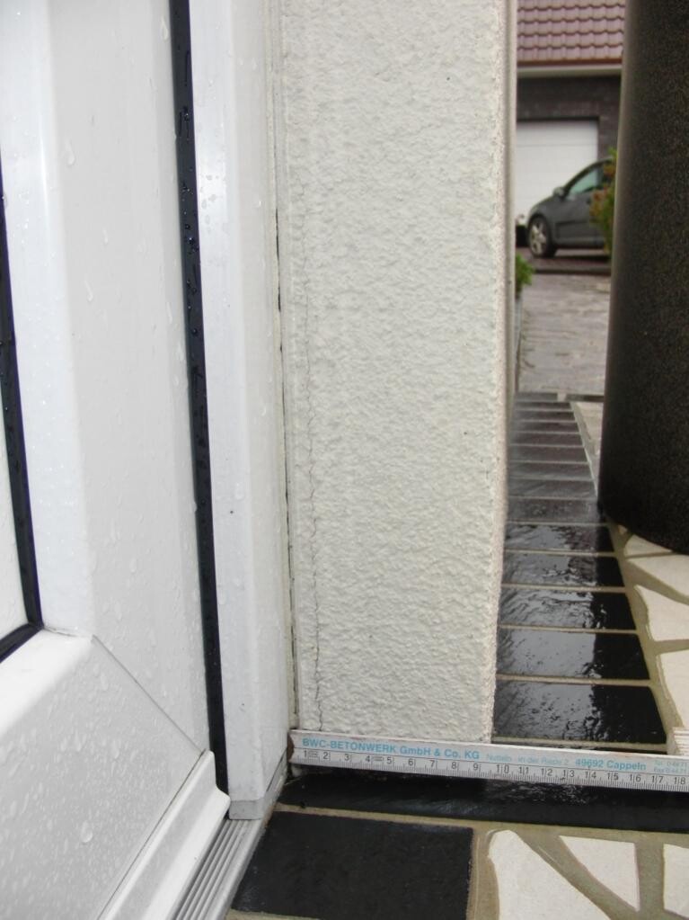 Exterior door frame with measuring tape on rain-wet ground outside.