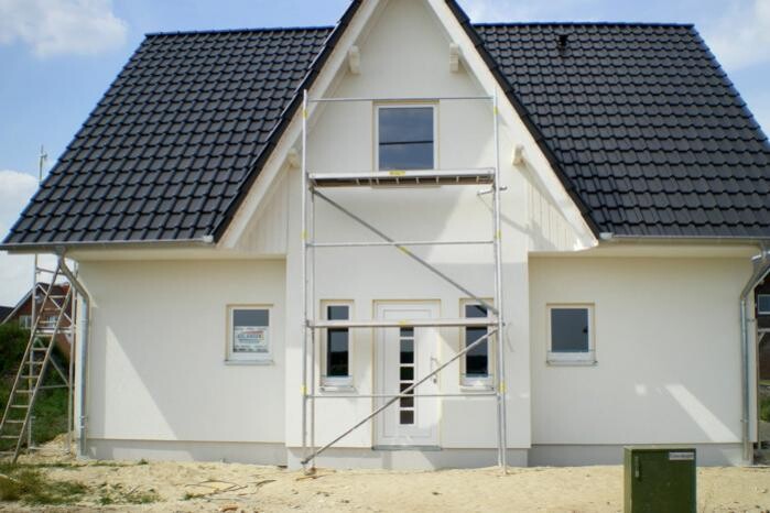 White single-family house with scaffolding in front of entrance and dark tiled roof.