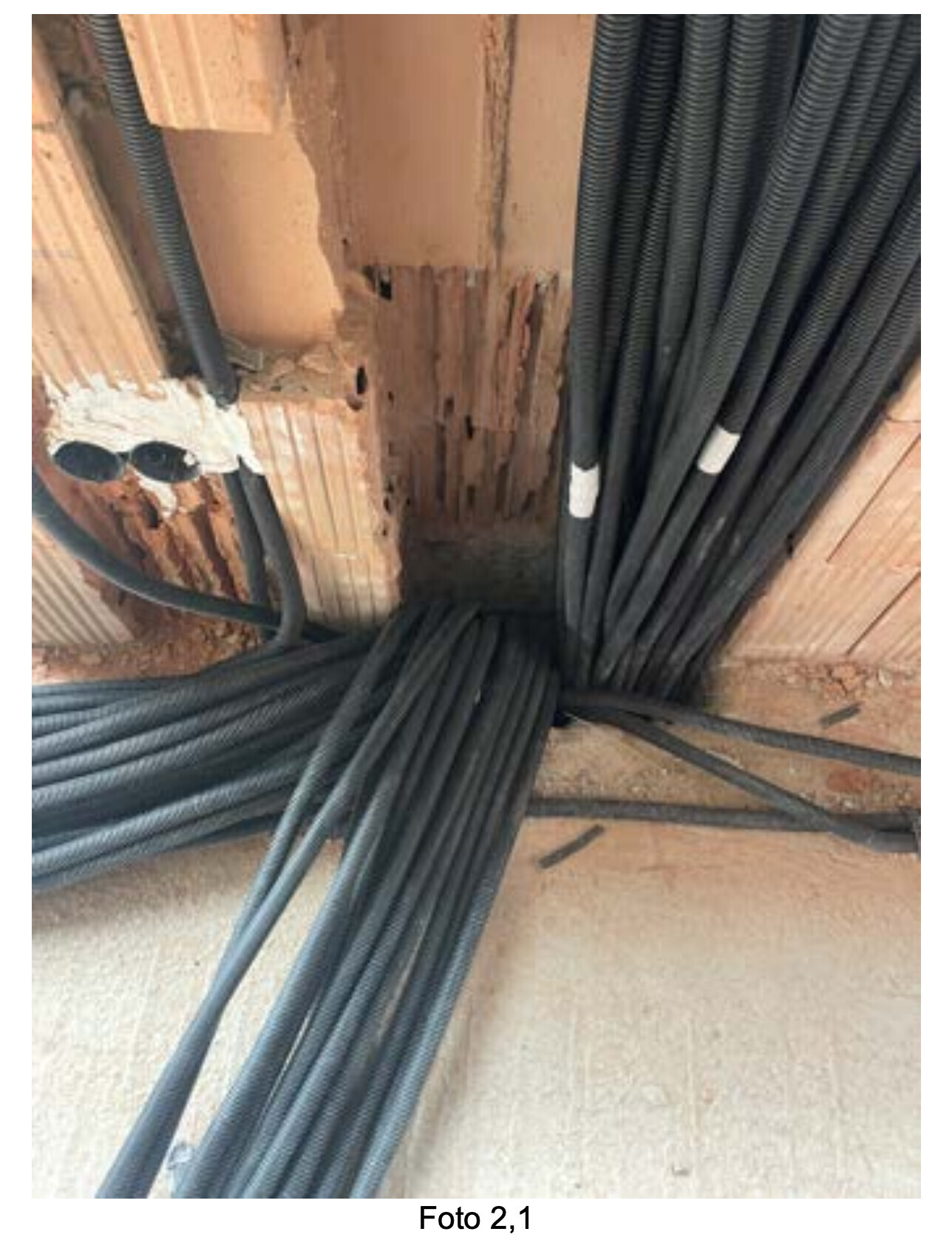 Many black cable bundles lying against a crumbling brick wall; cable ducts visible.