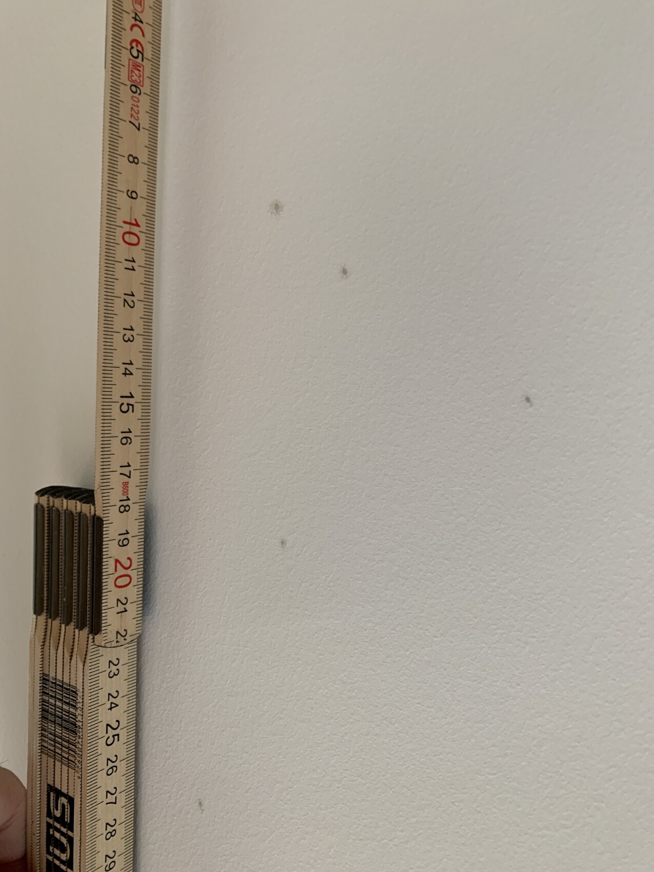 Tape measure on white wall during interior construction, small spots visible.