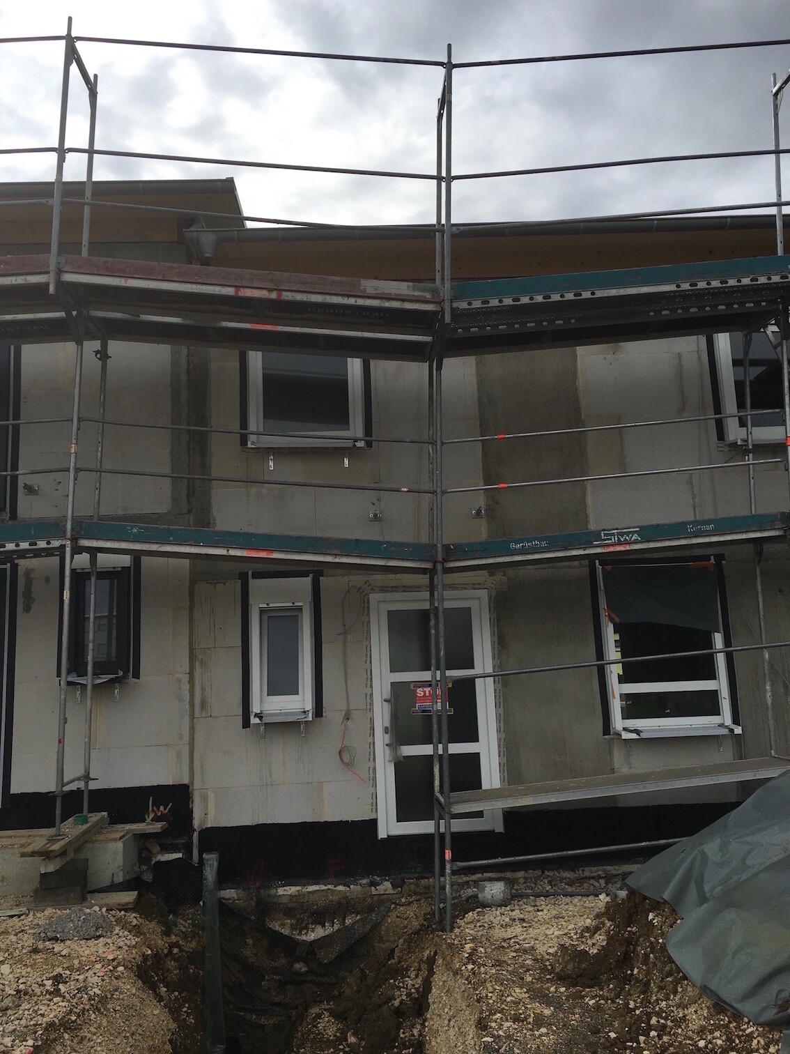 Unfinished house with scaffolding, window frames, and open earth trench