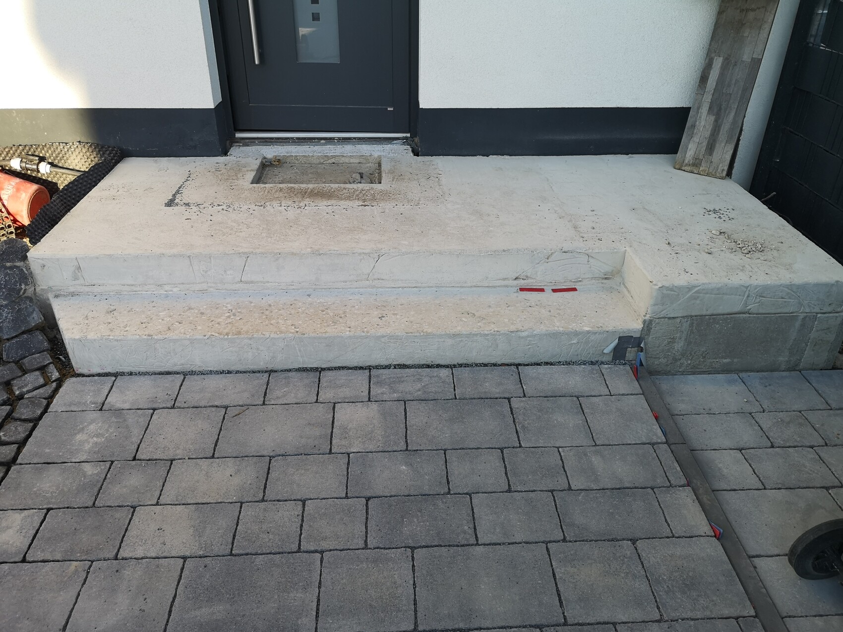 Concrete step in front of dark front door with rectangular recess; paved walkway in front.
