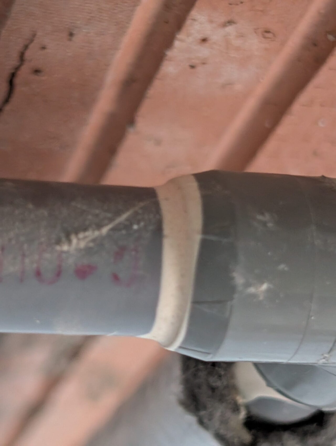Close-up of a black PVC pipe with beige clamp band, wooden background.