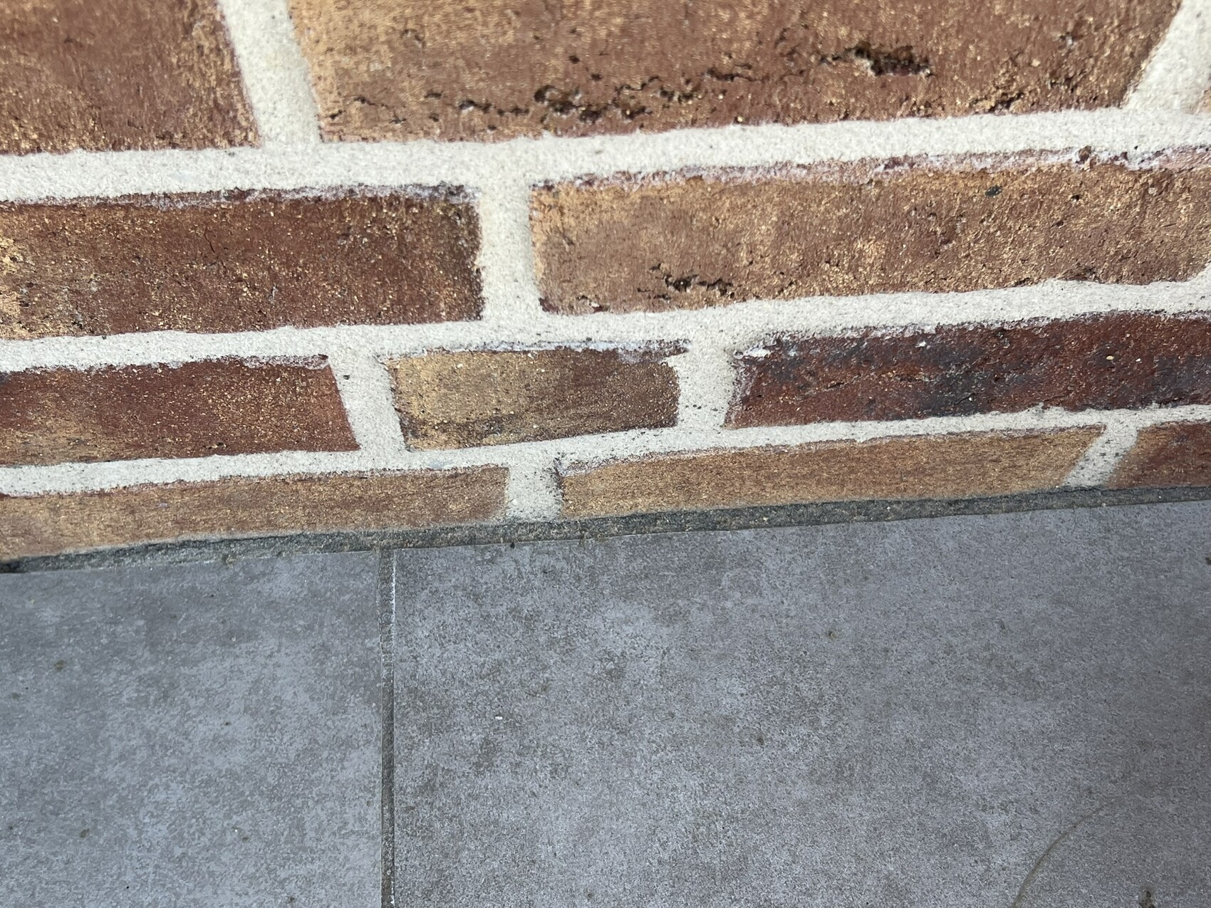 Nahaufnahme einer roten Backsteinwand mit hellgrauem Mörtel über einer grauen Bodenplatte.