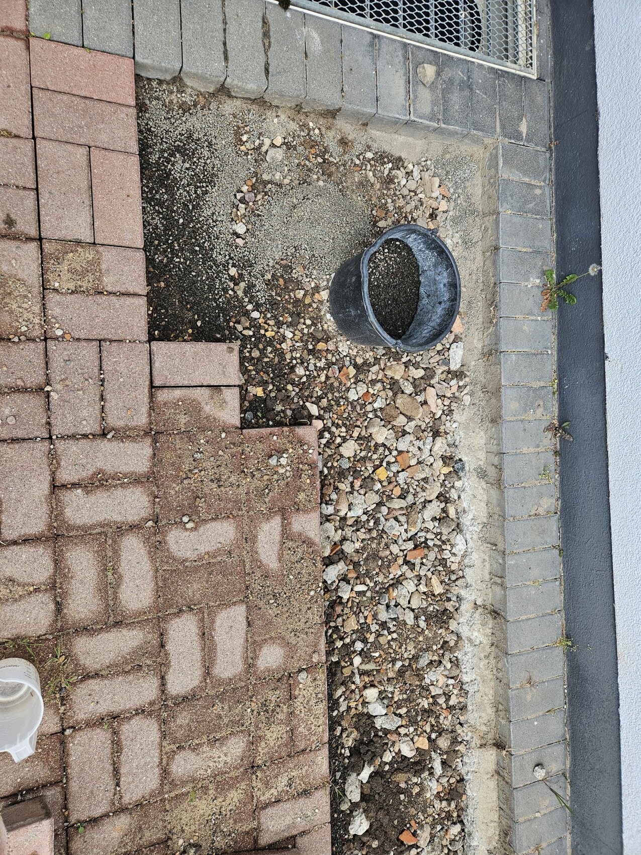 Outdoor area with paving stones, gravel and a pit next to the house wall.