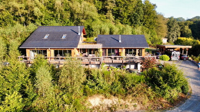 Exterior view of a modern wooden house in the woods with terrace and carport.