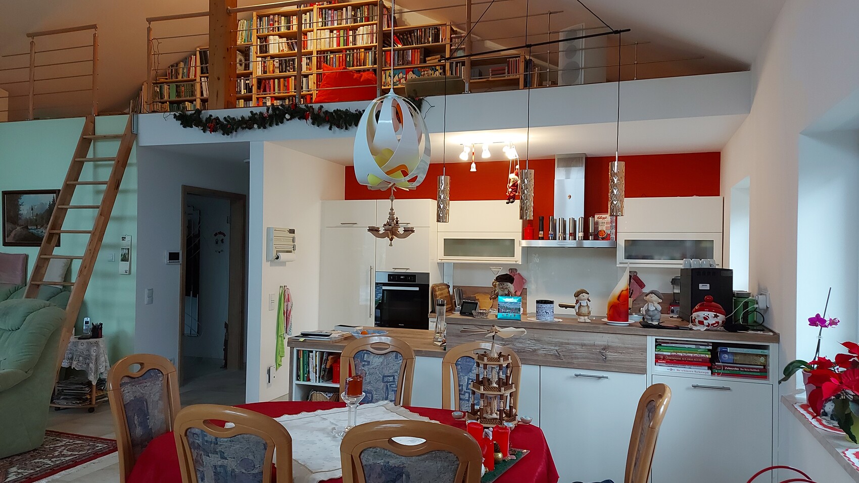 Open kitchen with dining table, stairs on the left, mezzanine bookshelf, and Christmas decorations.