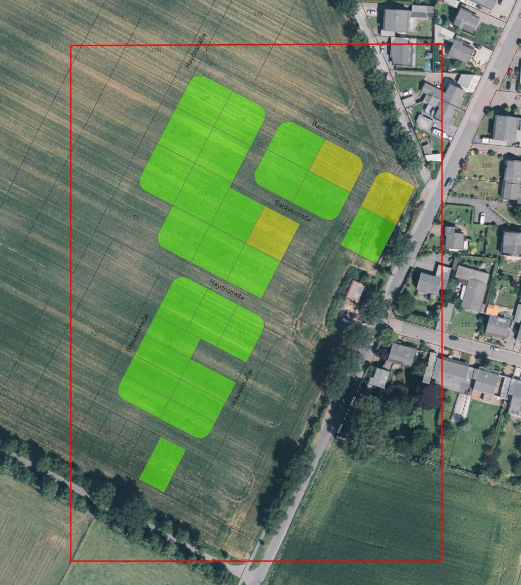 Aerial photo of a field area with green and yellow parcels outlined in a red frame next to a settlement.