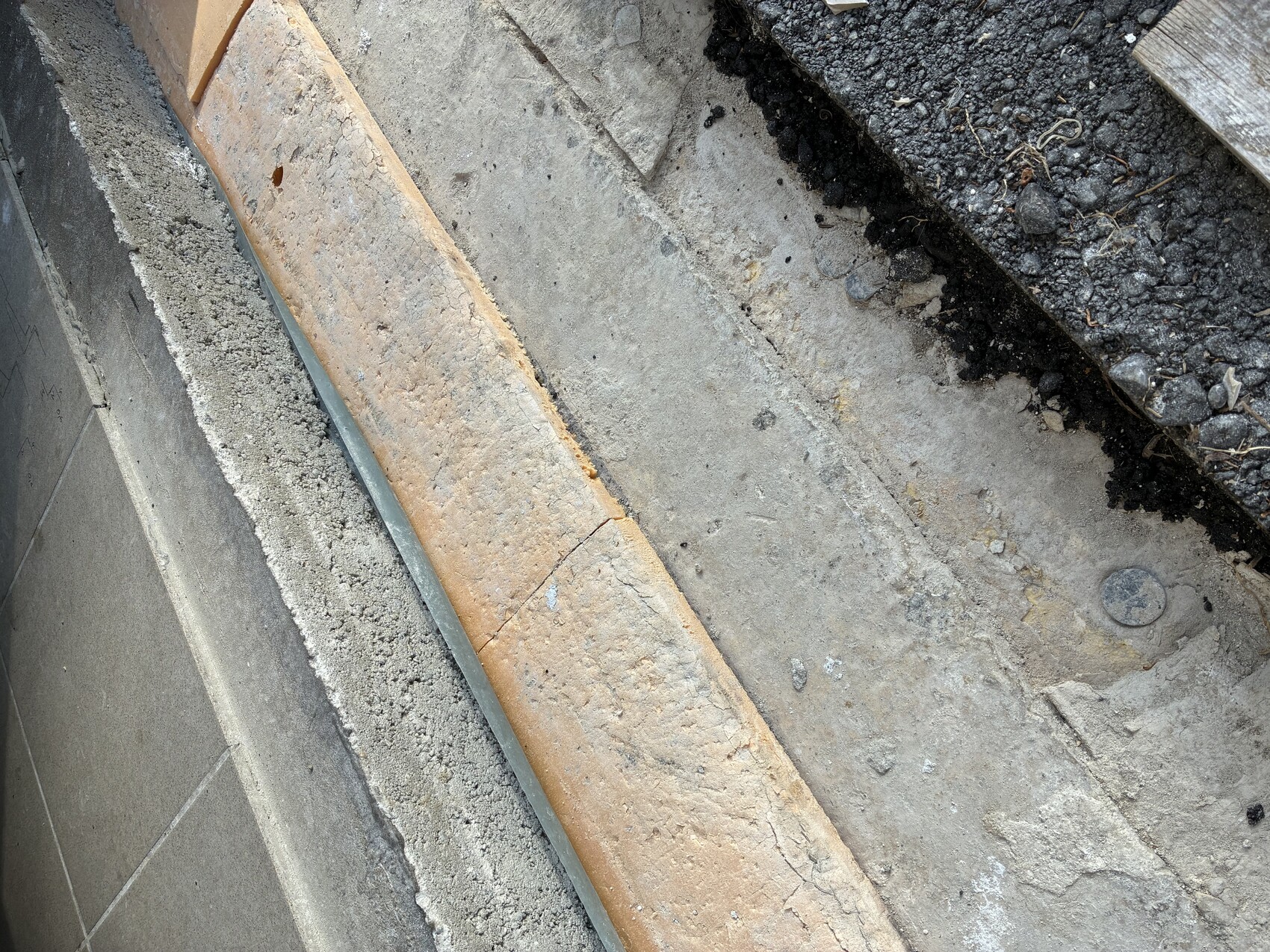 Gehwegkante mit bräunlicher Steinplatte, rissig, neben grauem Beton und Asphalt.