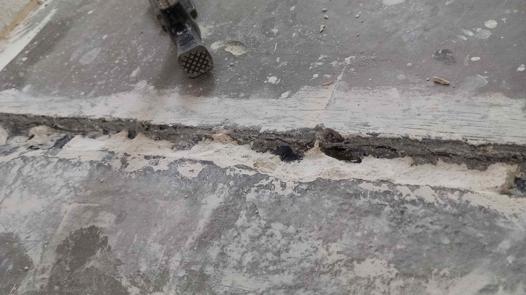 Broken edge of a concrete screed floor with dust, crack and small tool near the edge