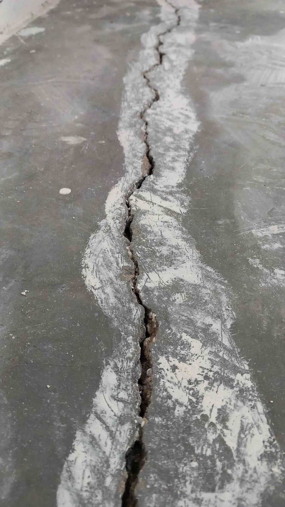 Cracked concrete floor with a long vertical gap and white dust
