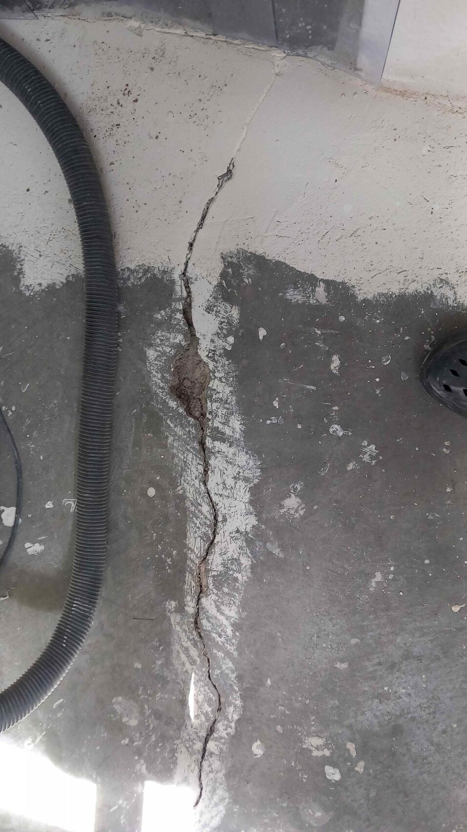 Large crack in a concrete floor slab, dark hose on the left, drain on the right.
