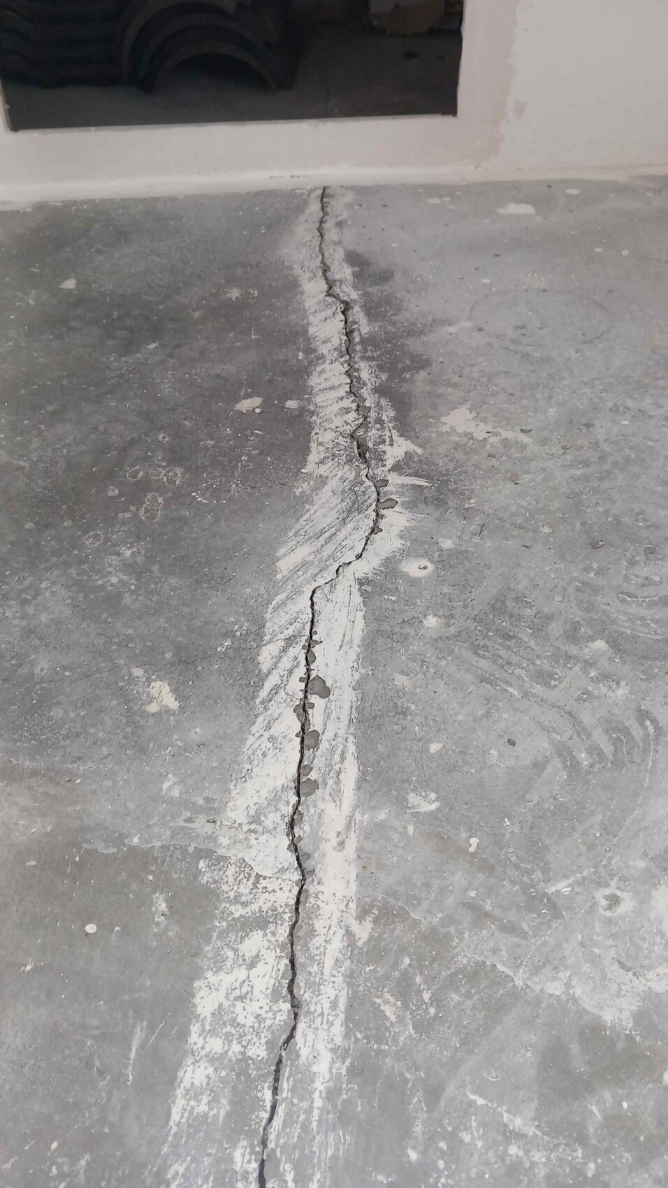 Wide crack in the concrete floor, running from foreground through the middle to the doorway.