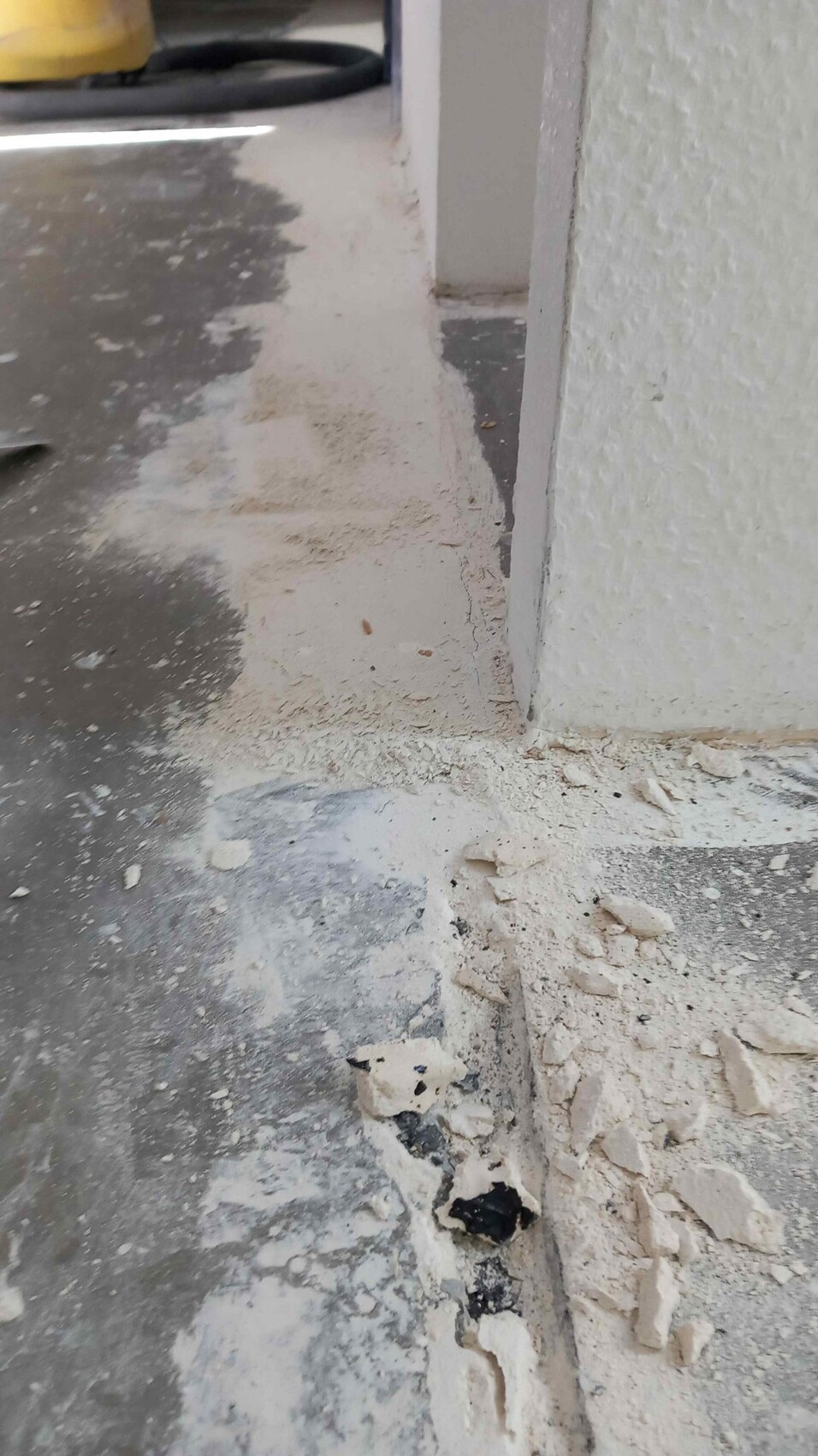 Construction scene with dust, plaster remains and crumbly floor edge next to a white wall.