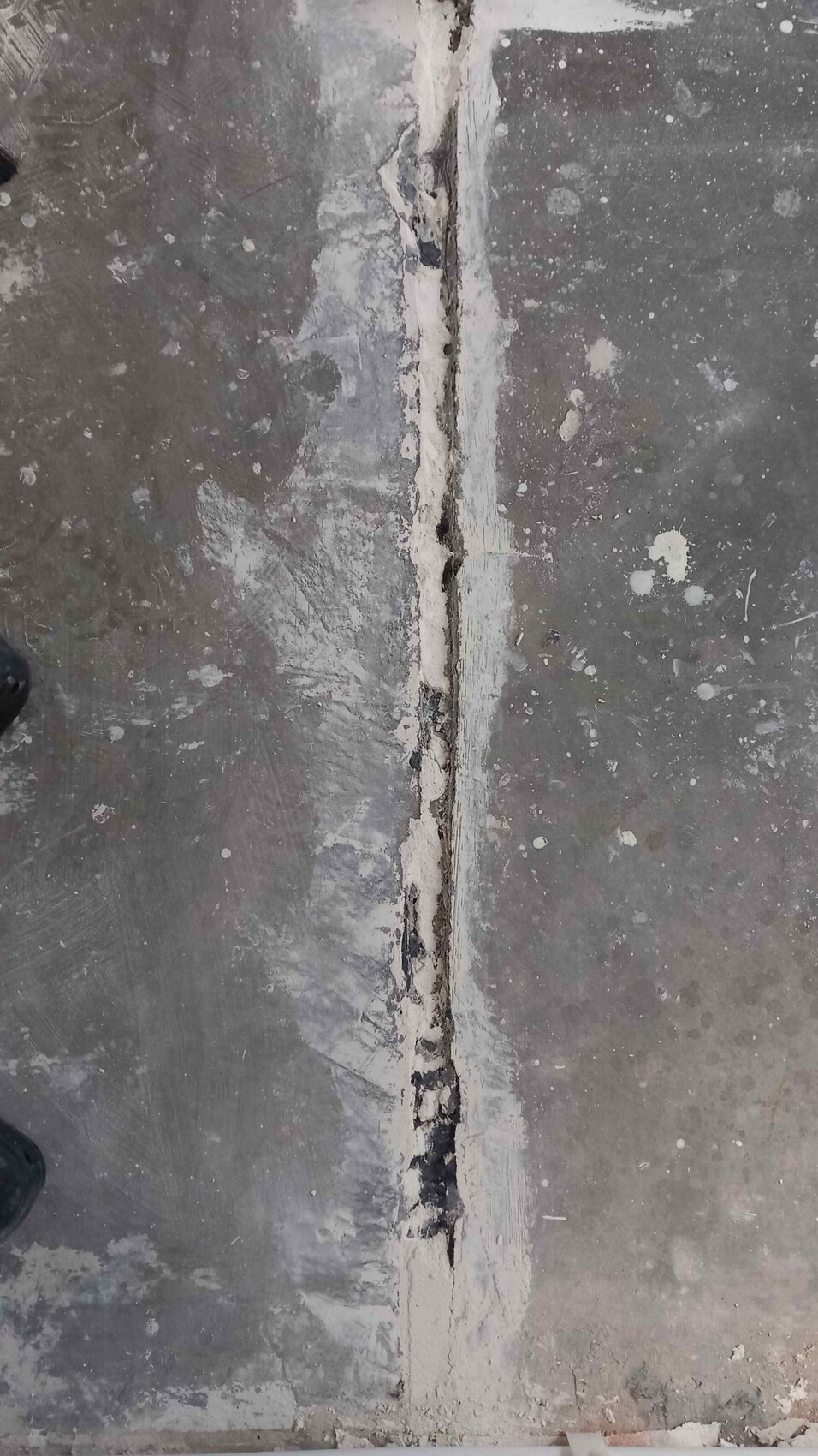 Concrete floor with vertical crack in the middle, surrounded by sealant.