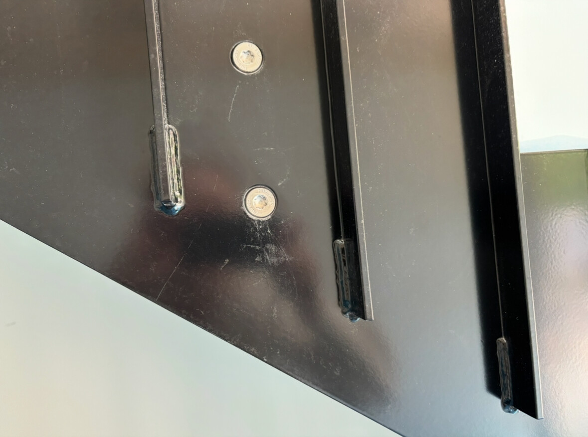 Close-up of a black metal fitting with screws and guide rails.