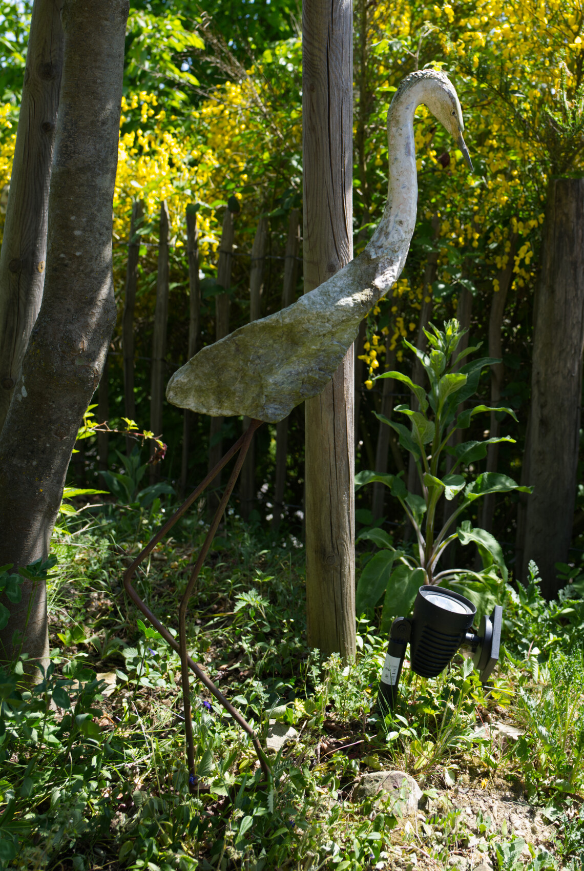 Weathered bird sculpture in the garden next to a ground light
