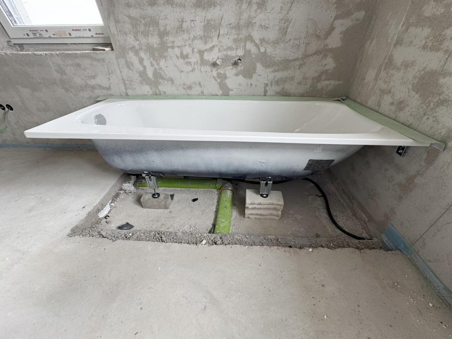 Bathtub being installed in unfinished bathroom, visible raw walls and plumbing pipes.