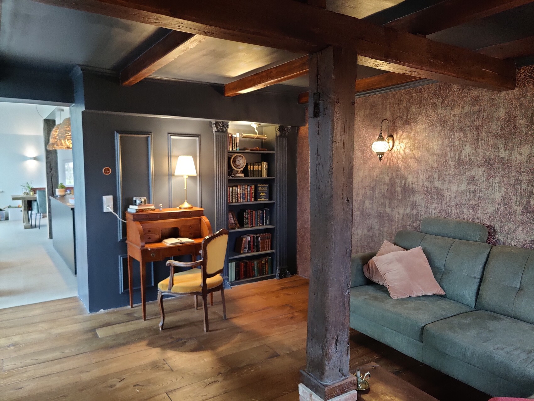 Living room with exposed wooden beams, desk, bookshelf, and teal sofa.