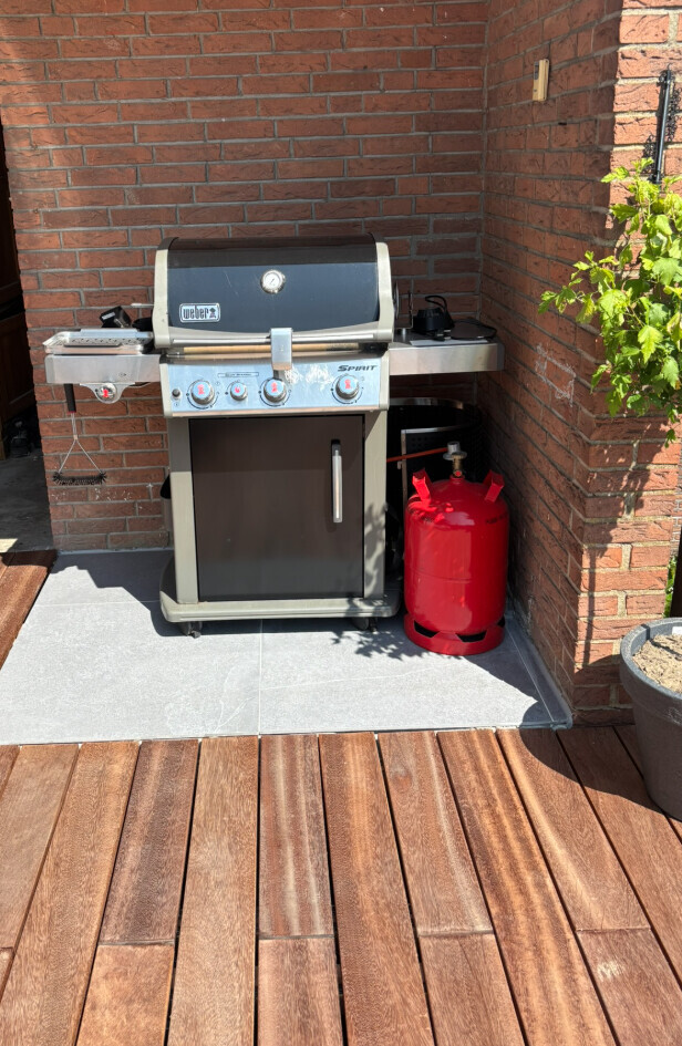 Weber Spirit gas grill on terrace next to red propane tank in front of brick wall.
