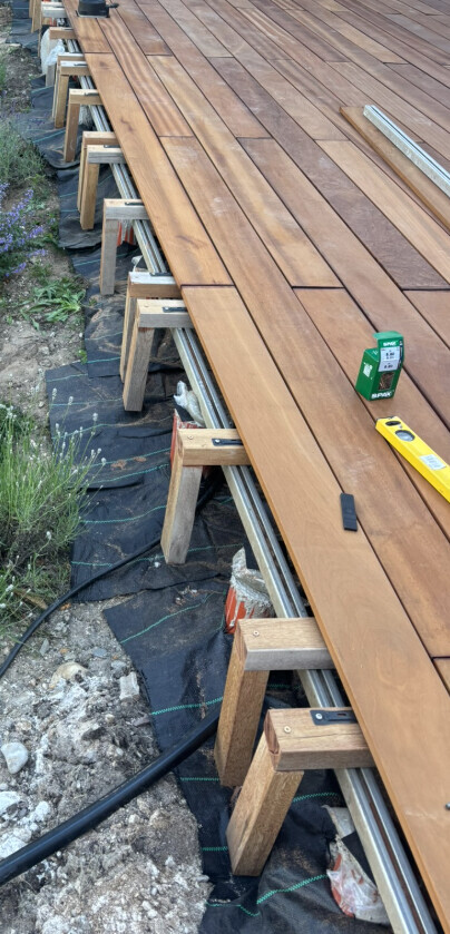 Wooden deck under construction: long decking boards on substructure made of wooden beams; measuring tool ready.