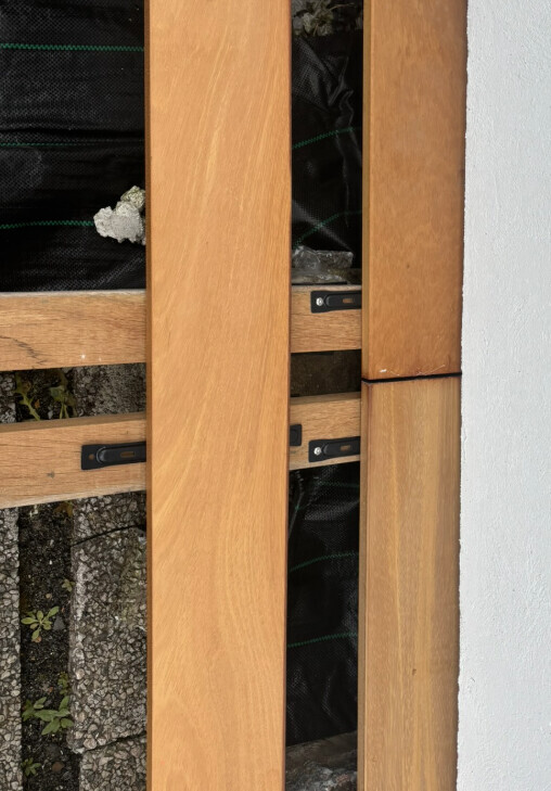 Vertical wooden boards form a frame in front of a white wall; building wrap is visible behind.
