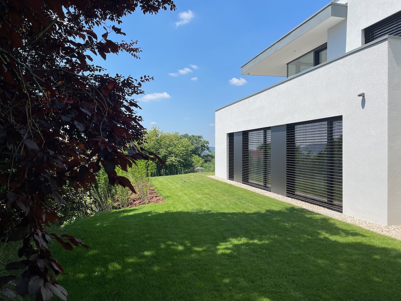 Modern white house facade with large windows and black shutters, green lawn.