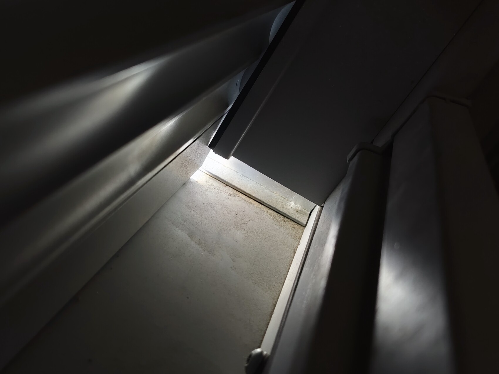 Close-up of a dark metallic interior with a narrow light gap and dust on surfaces