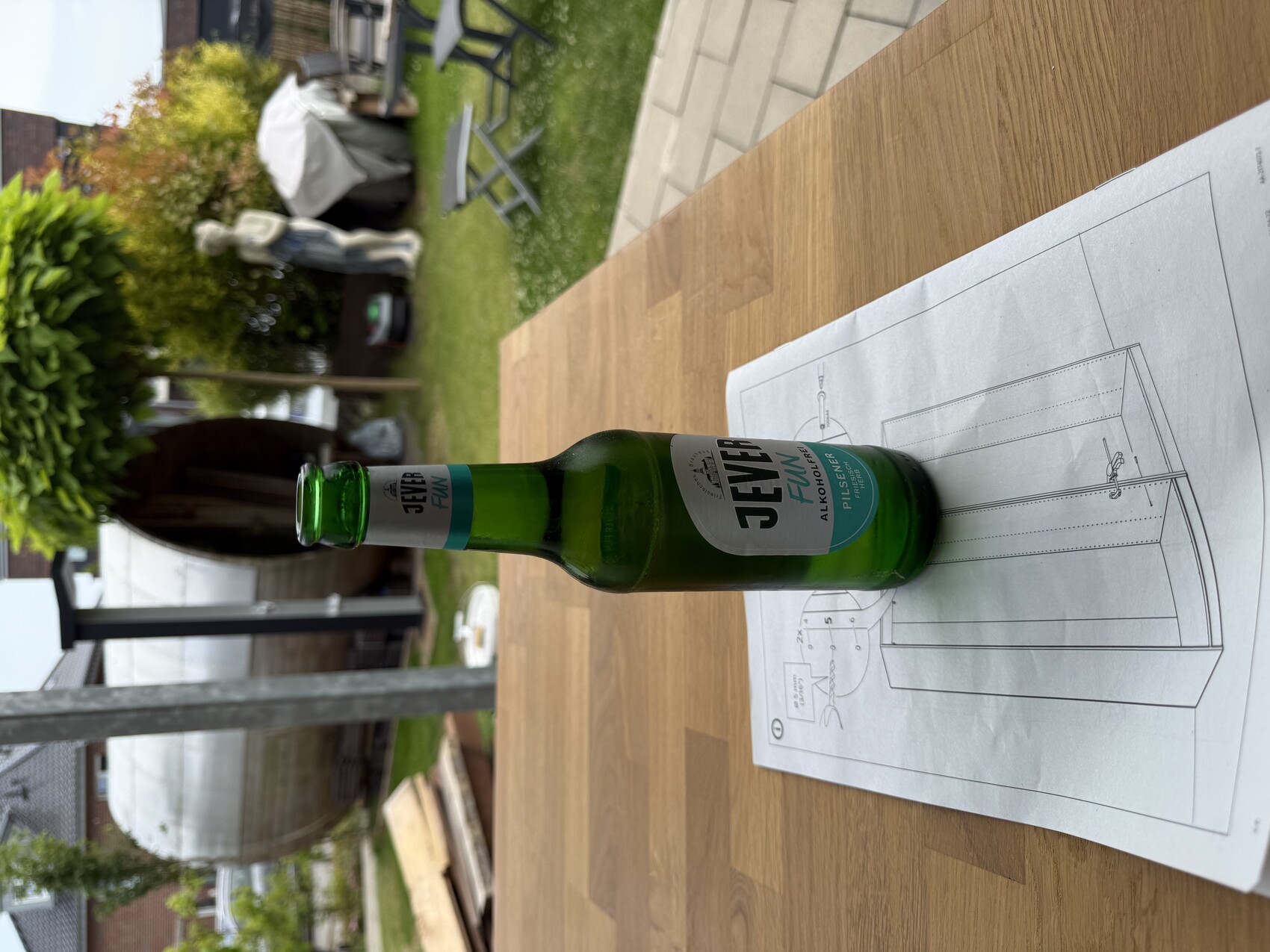 Grüne Jever Fun alkoholfreie Bierflasche steht auf Bauplan auf Holztisch im Garten.