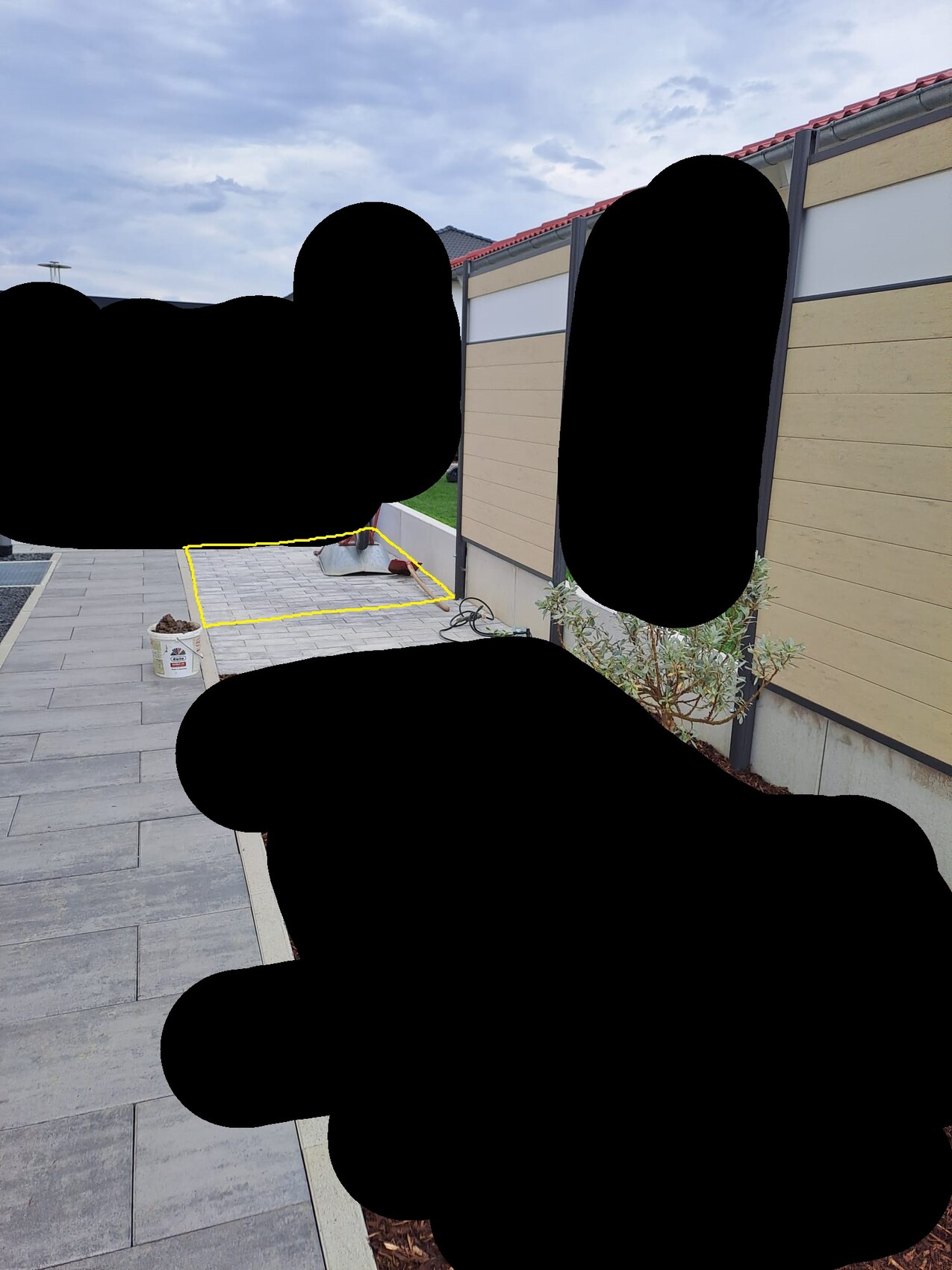 Gepflasterte Terrasse neben einer Gebäudewand; gelb markiertes Quadrat mit Werkzeugen.