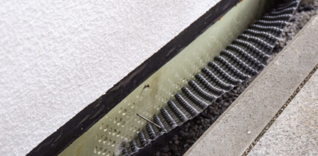 Exterior wall area with green stud drainage and edge strip next to concrete path.