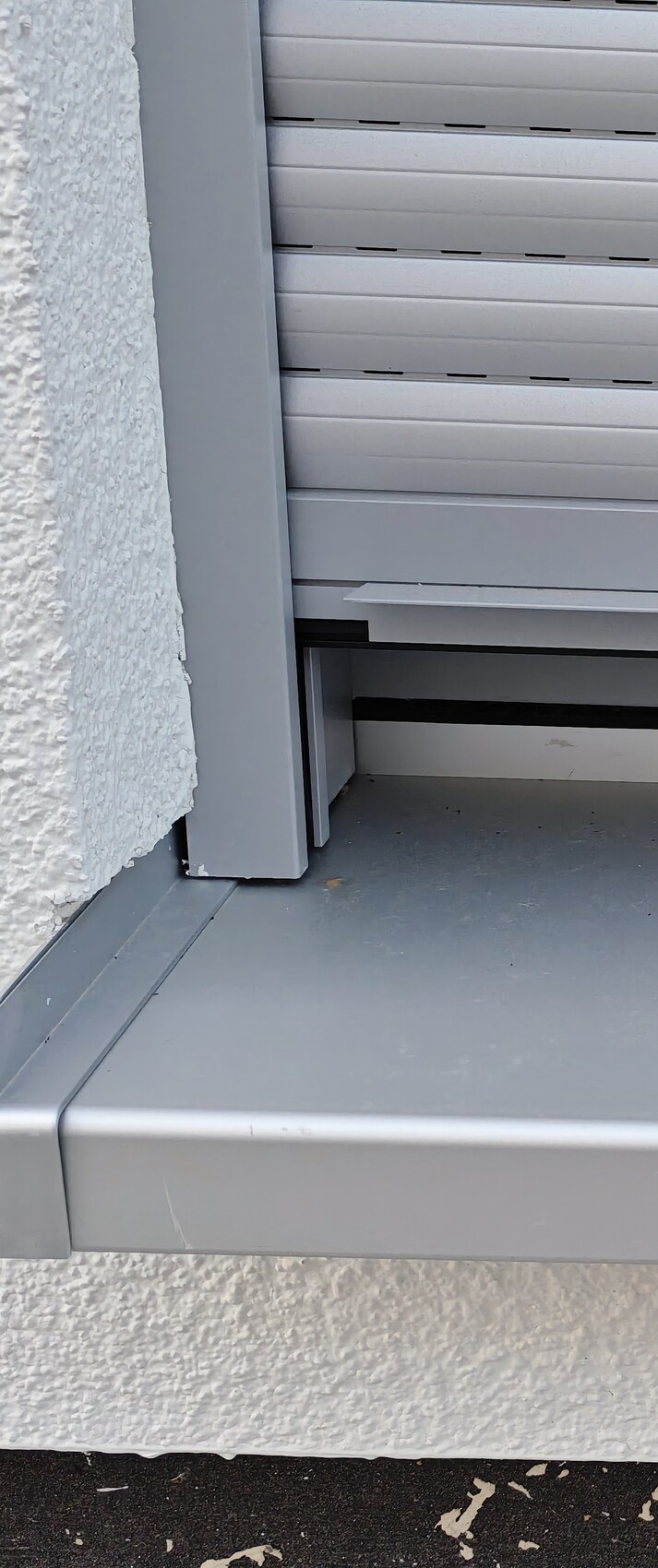 Gray roller shutter in front of white, textured exterior wall; close-up