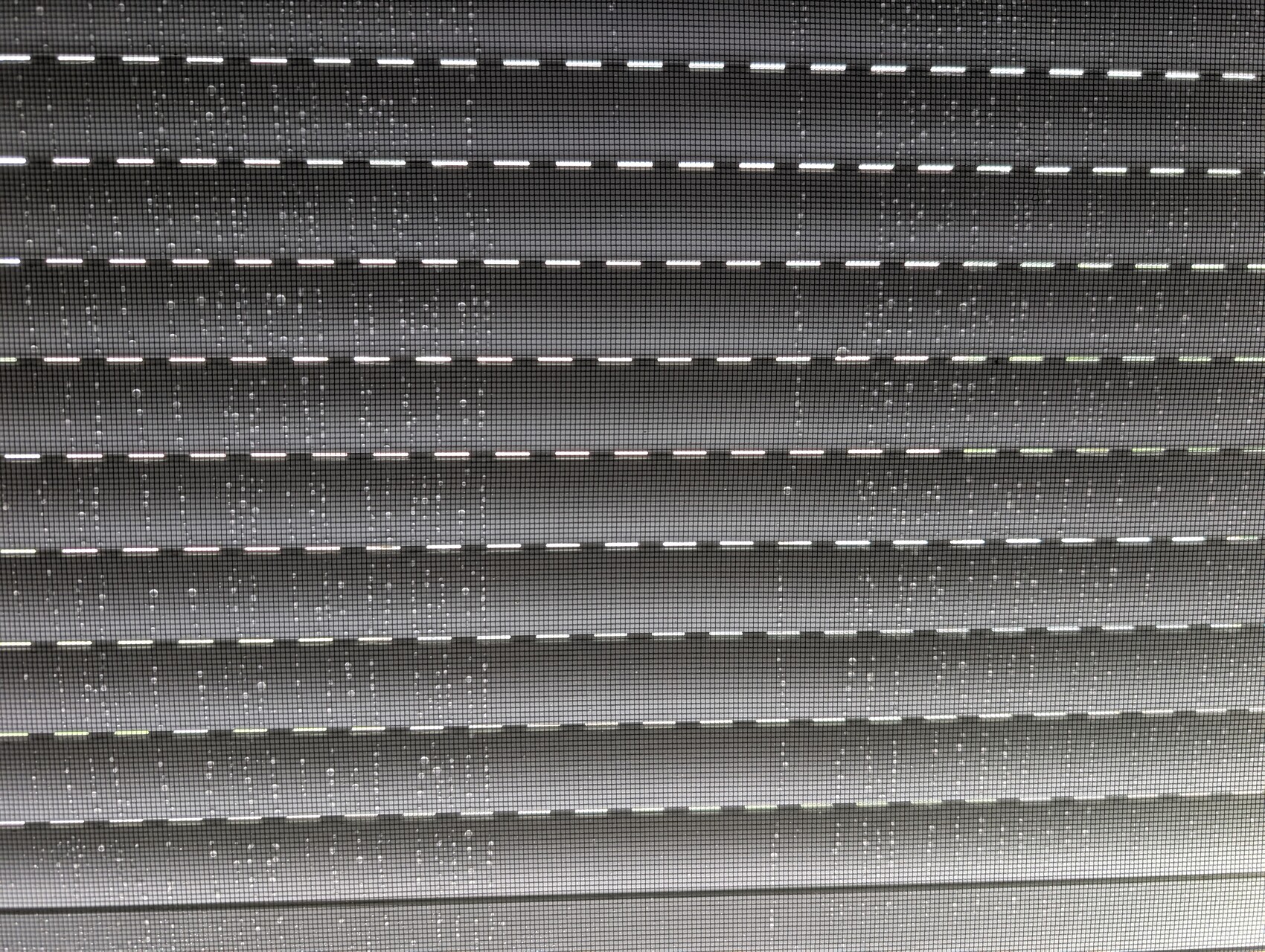 Close-up of gray horizontal blinds with regular slats, light shining through.