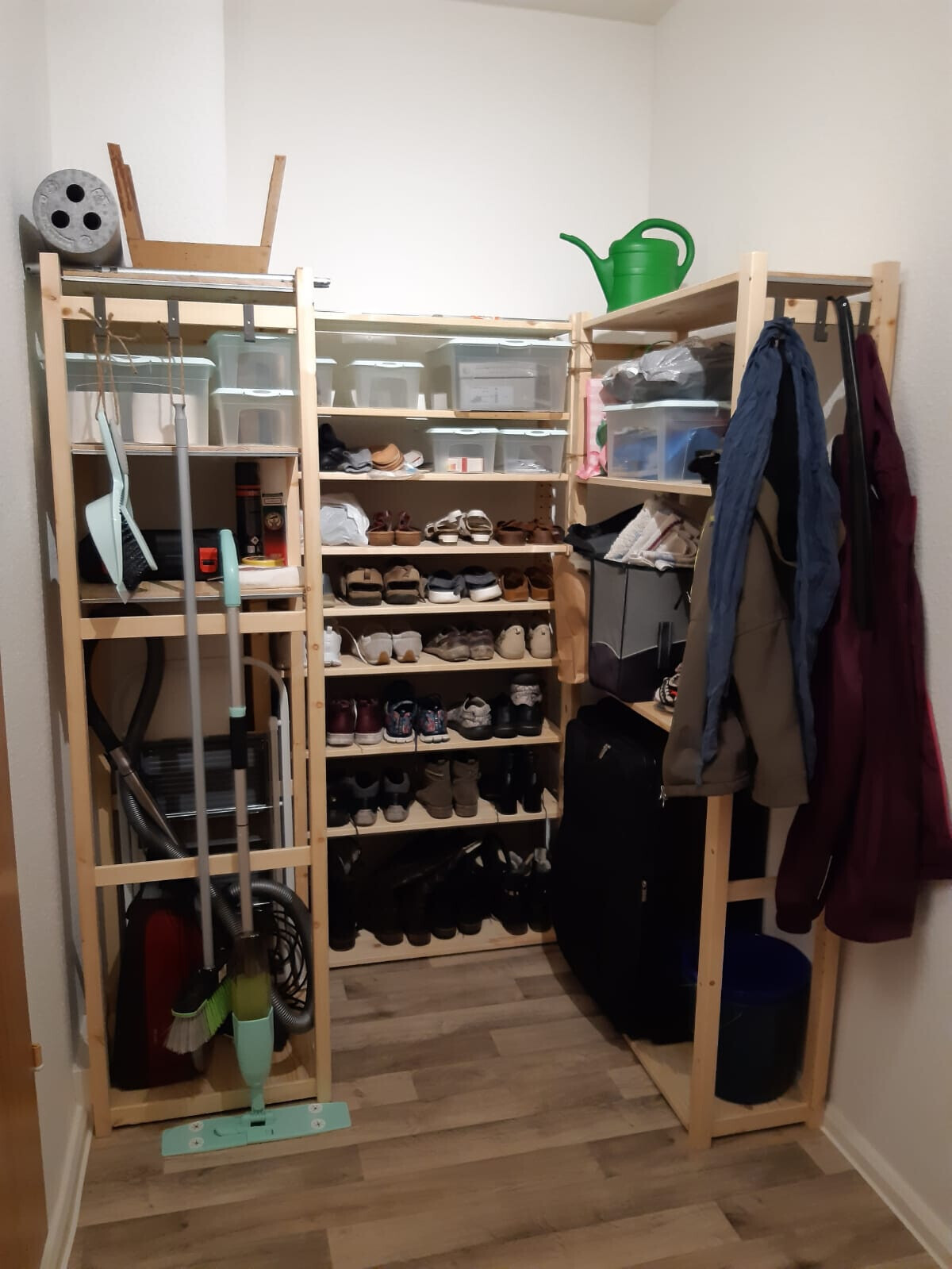 Open wooden cabinet with shoe racks, storage boxes, jackets, and cleaning tools.