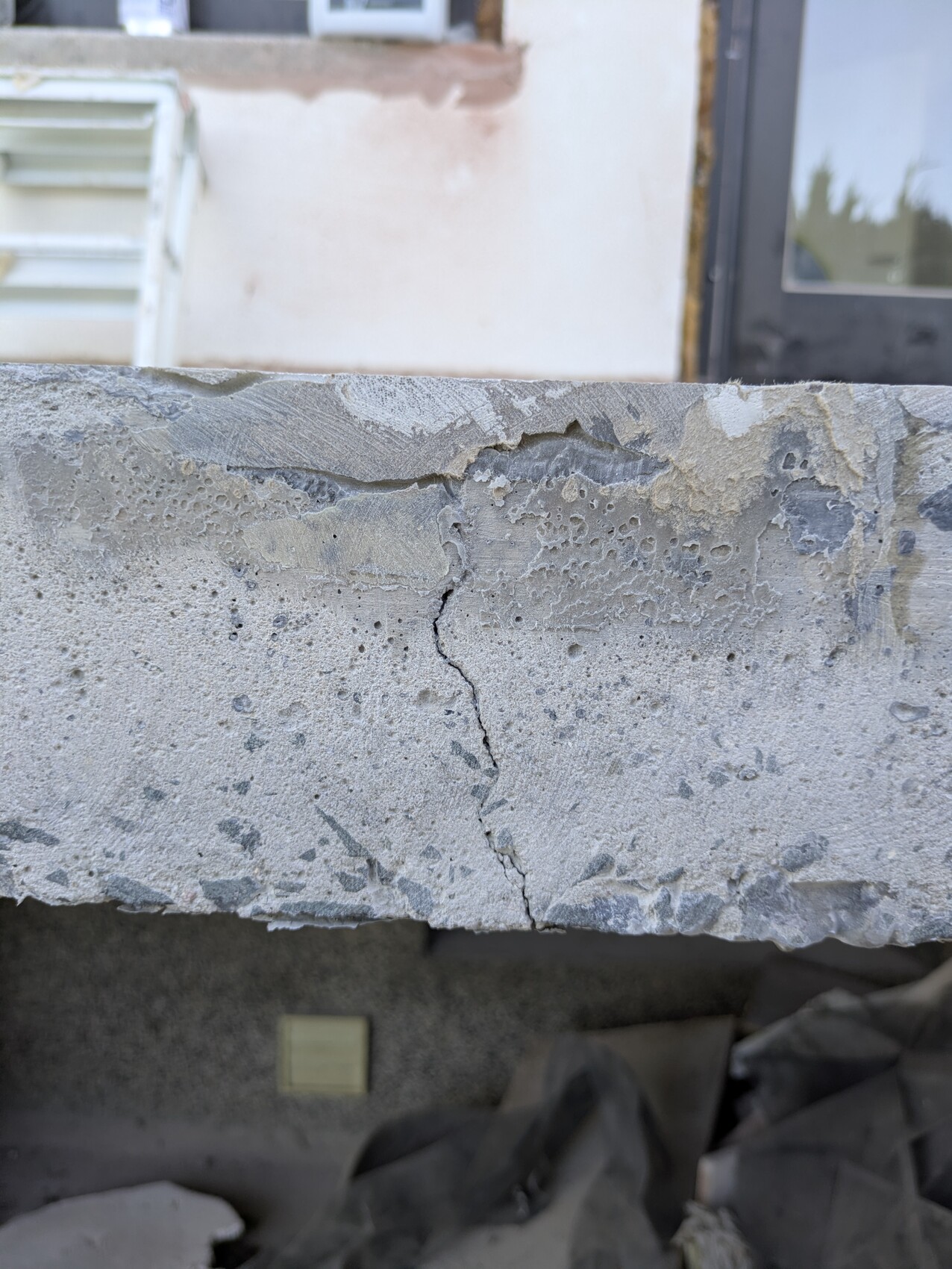 Close-up of a rough concrete slab with a crack, background: building with window.