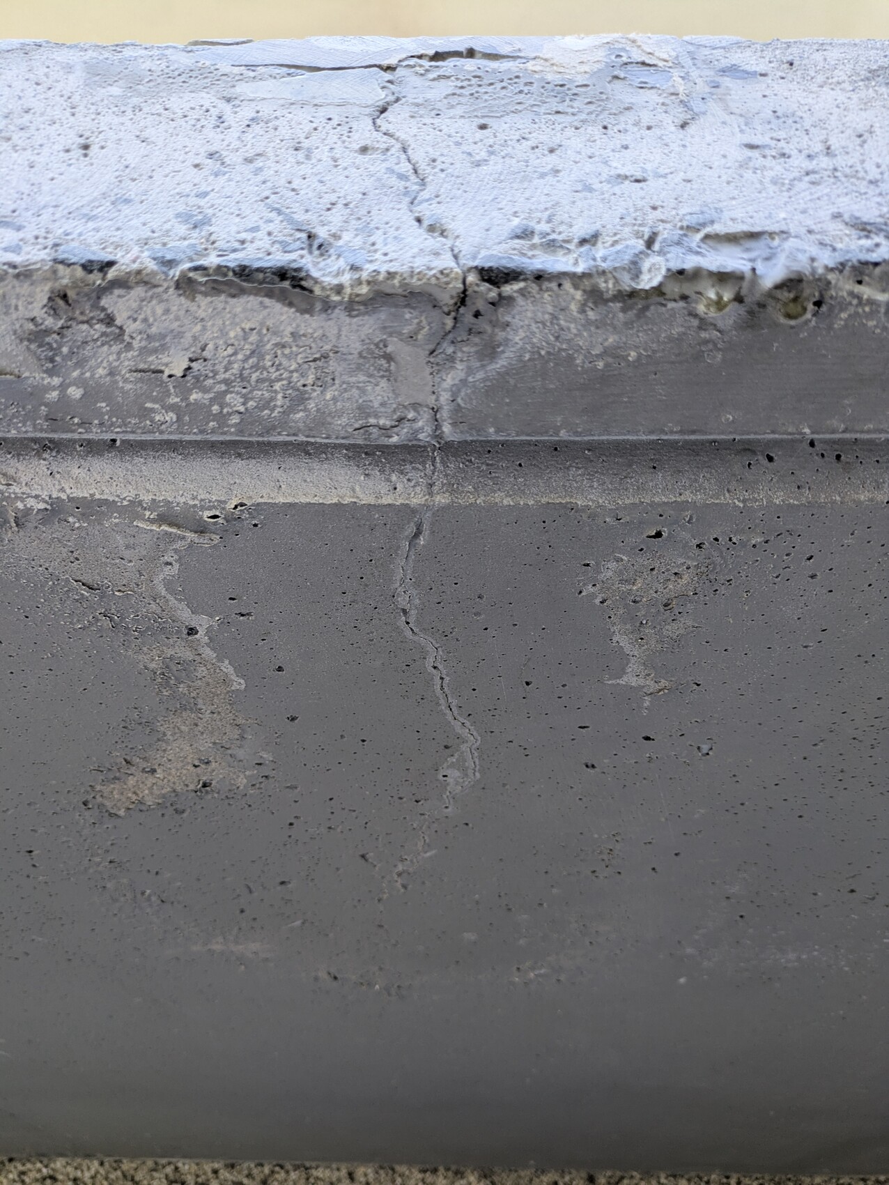 Close-up of a concrete wall with vertical crack and rough upper edge.