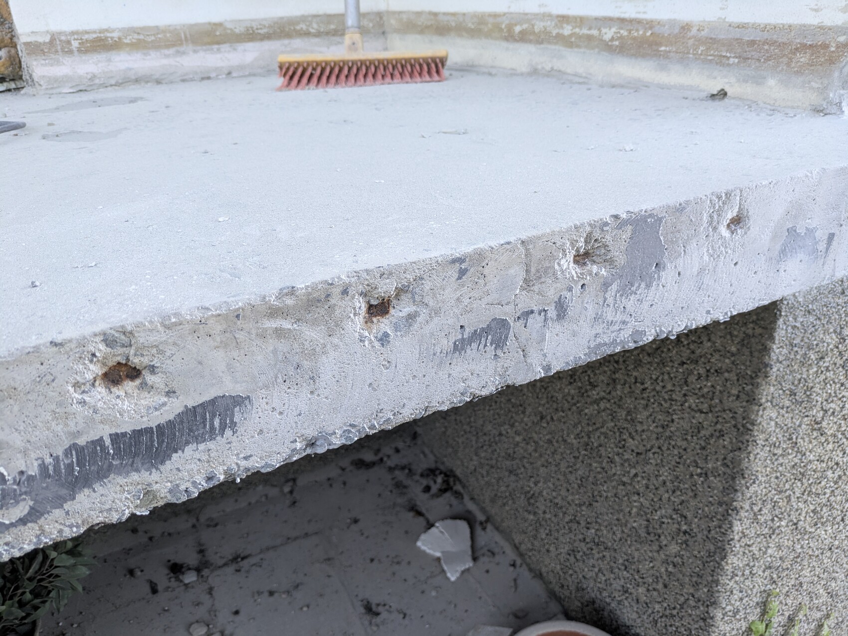 Exterior concrete slab with rough edge; red broom lies on it.