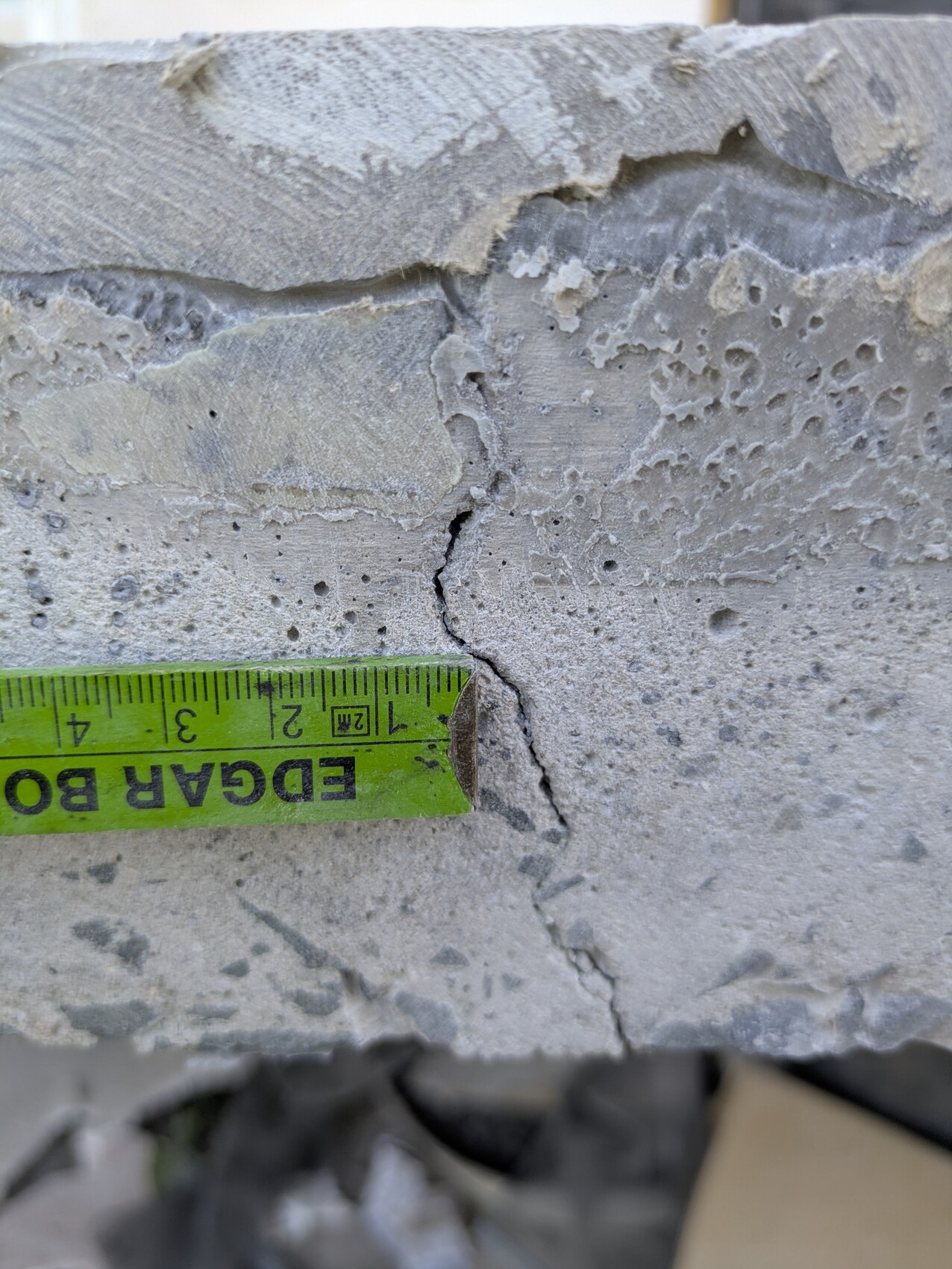 Close-up of a rough concrete surface with a crack; a green measuring tape lies across