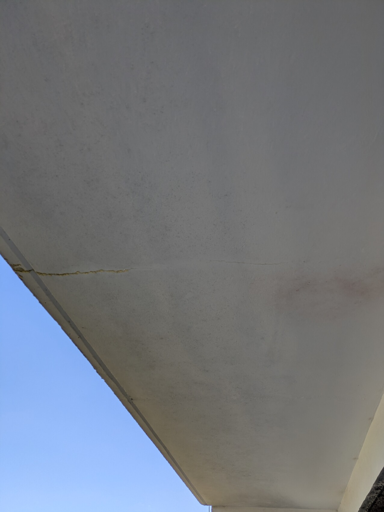 Underside of a concrete balcony with crack, blue sky in the background.