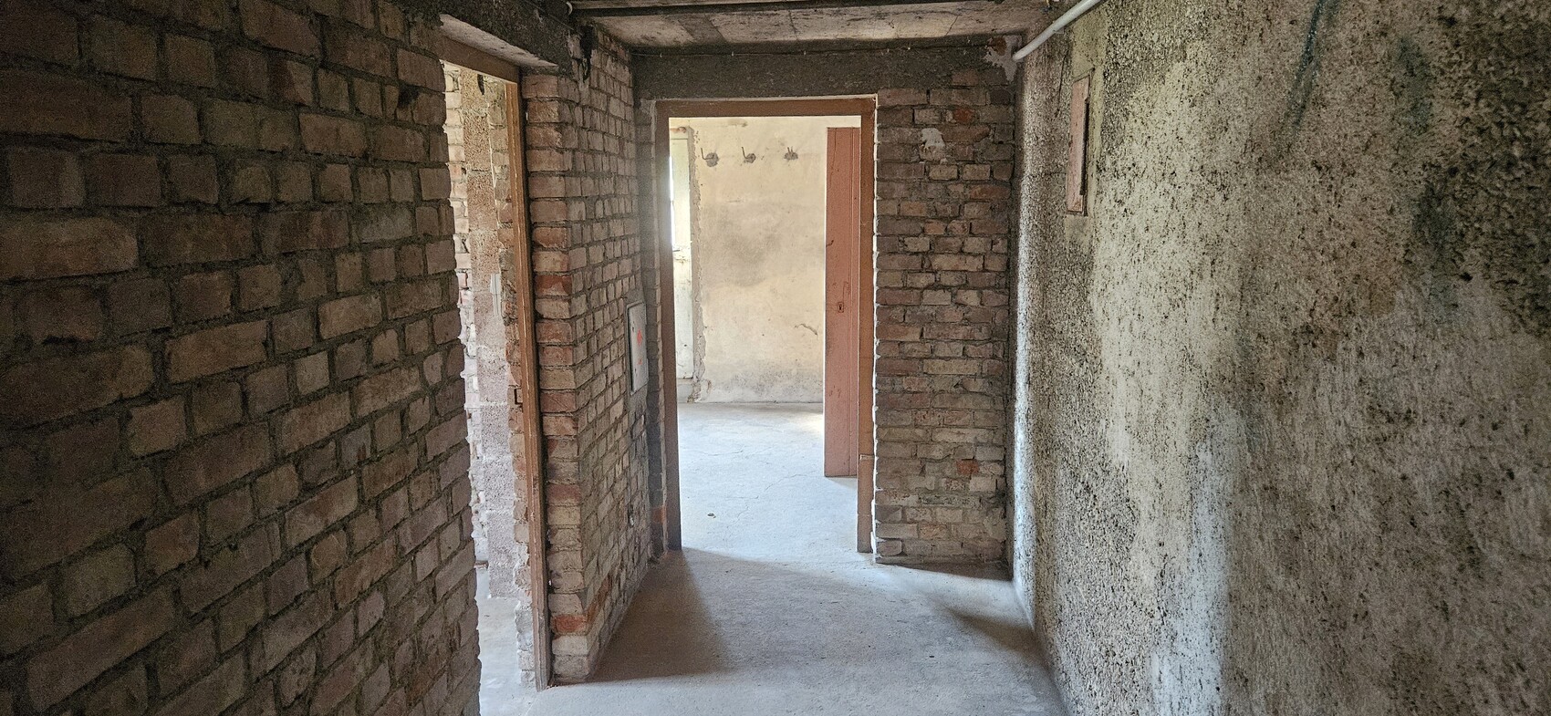 Interior view of an unfinished building: brick walls, doorways, rough concrete floor