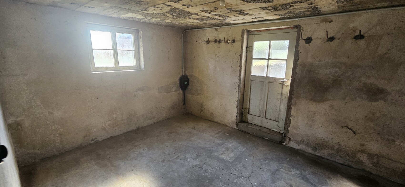 Concrete basement room with small window, door, hook rack and old electrical box